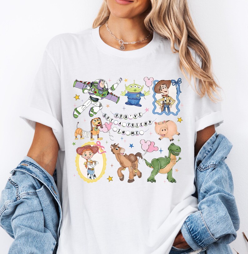 May include: White t-shirt featuring colorful cartoon characters from the Toy Story movie. The design includes Buzz Lightyear, Woody, an alien, and the text "You've Got a Friend in Me."