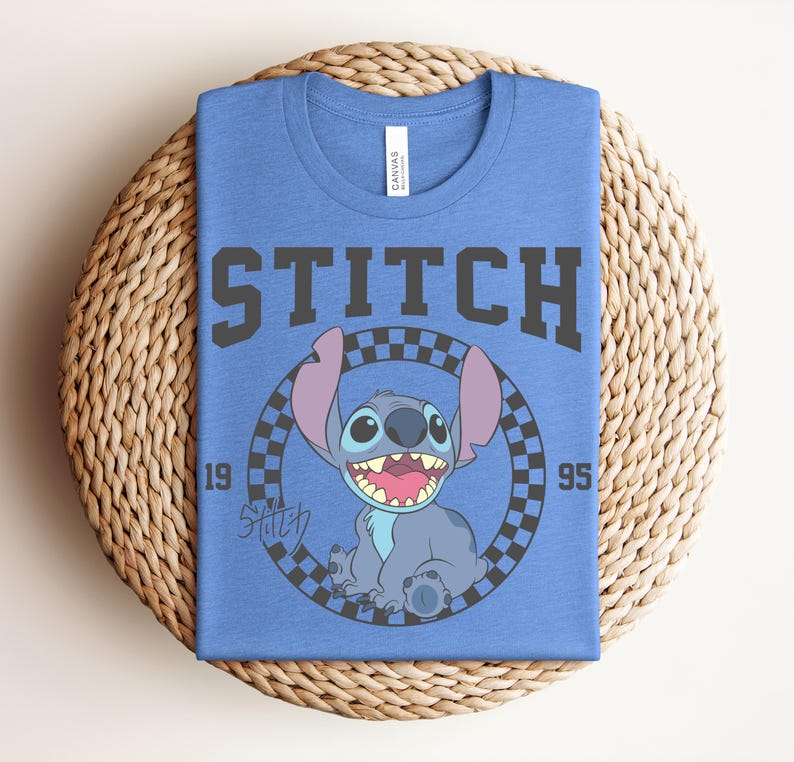 May include: Blue t-shirt featuring a graphic of Stitch from Lilo & Stitch. The design includes the word "STITCH" in bold, gray letters above a circular image of Stitch. The image is surrounded by a checkered pattern, with the numbers "19" and "95" on either side.
