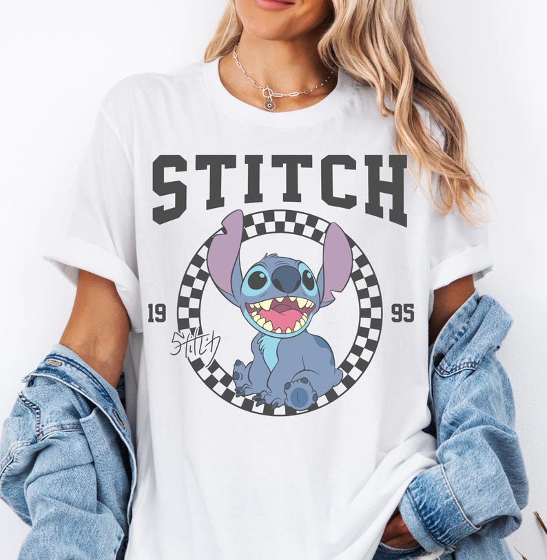 May include: White t-shirt featuring a graphic of Stitch from Lilo & Stitch. The design includes the word "STITCH" in bold, black letters above a circular image of Stitch. The image is surrounded by a black and white checkered pattern, with the numbers "19" and "95" on either side.