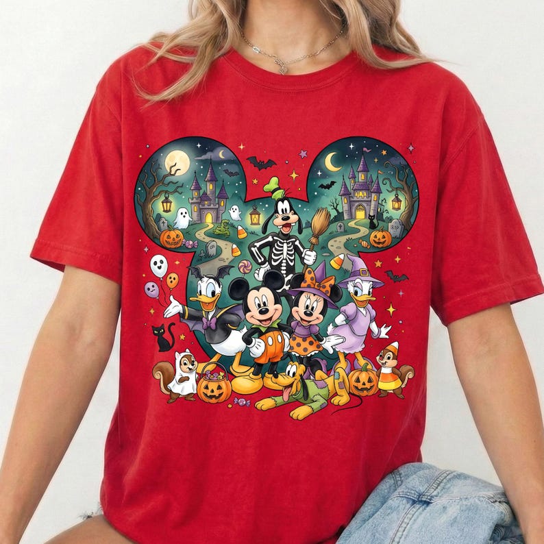 K&ouml;nnte beinhalten: Ein rotes T-Shirt mit einer gro&szlig;en Grafik in Form von Mickey-Mouse-Ohren, die eine Halloween-Szene zeigt. Das Design enth&auml;lt Zeichentrickfiguren in Kost&uuml;men, ein Spukschloss, K&uuml;rbisse, Geister, Flederm&auml;use und einen Mond vor einem dunklen Nachthimmel.