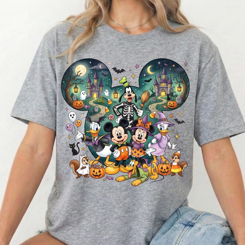 K&ouml;nnte beinhalten: Ein graues T-Shirt mit einem gro&szlig;en, Mickey-Maus-f&ouml;rmigen Aufdruck, der eine Halloween-Szene zeigt. Das Motiv enth&auml;lt Zeichentrickfiguren in Kost&uuml;men, K&uuml;rbisse, Geister, Flederm&auml;use und ein Schloss vor einem dunklen Nachthimmel.