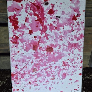 May include: Abstract canvas art with a white backdrop and splashes of pink and red paint. The artwork features a mix of small and large paint splashes, creating a dynamic and expressive composition. Signed by the artist.