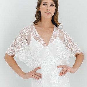 May include: A white lace dress with a V-neckline and short sleeves. The dress has a flowing skirt and a fitted bodice.