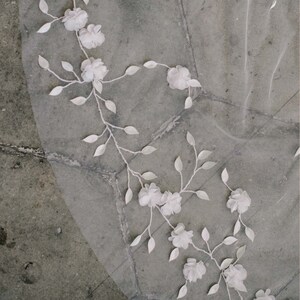 May include: White floral applique on a sheer white veil. The floral design features delicate white flowers and leaves.
