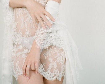 May include: A sheer white lace slip with delicate floral patterns. The slip has thin straps and a flowing skirt.