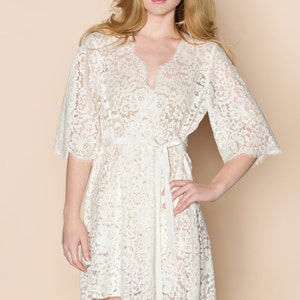 May include: A white lace robe with a V-neckline and 3/4 sleeves. The robe has a tie at the waist and a scalloped hem.