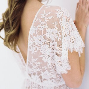 May include: A white lace top with a deep V-neckline and short sleeves. The lace is delicate and intricate, with a floral pattern.