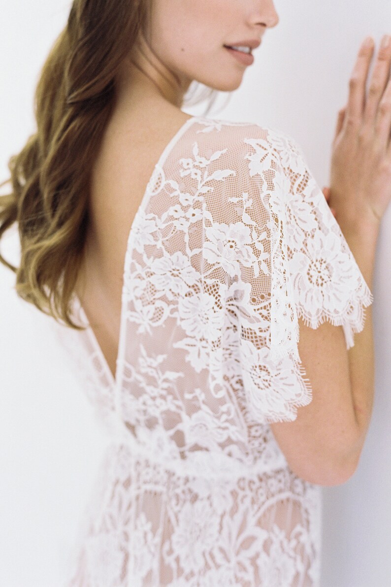 May include: A white lace top with a deep V-neckline and short sleeves. The lace is delicate and intricate, with a floral pattern.