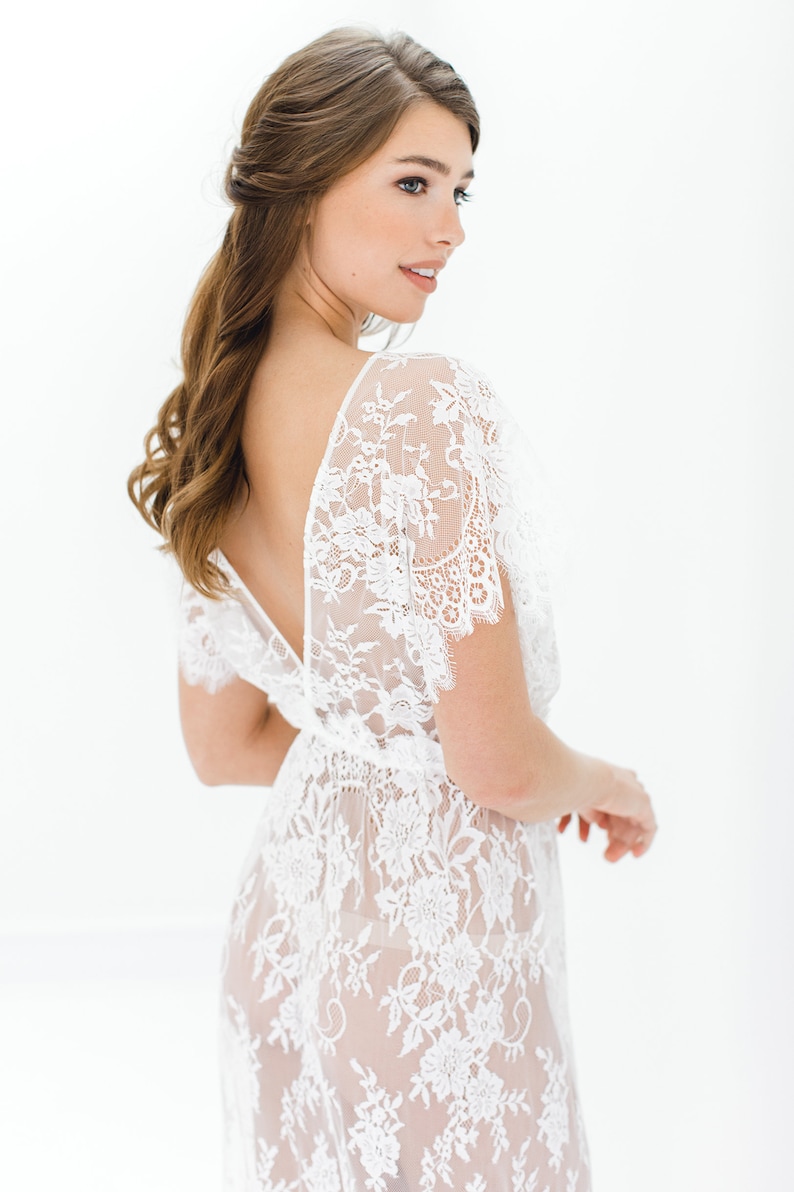 May include: A white lace dress with a deep V-neckline and short sleeves. The dress is sheer and has a floral pattern.
