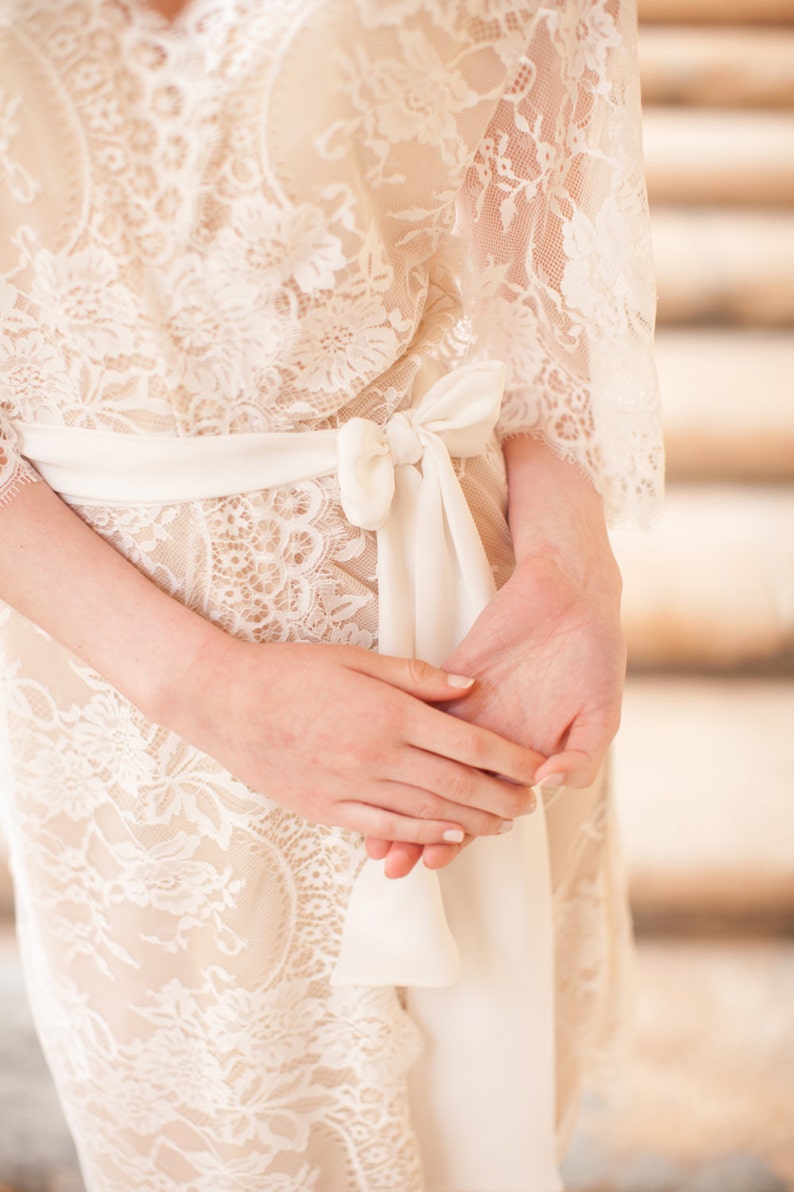 Puede incluir: Una bata de encaje blanco con una cinta de sat&eacute;n atada a la cintura. La bata es delicada y femenina, con una tela suave y fluida.