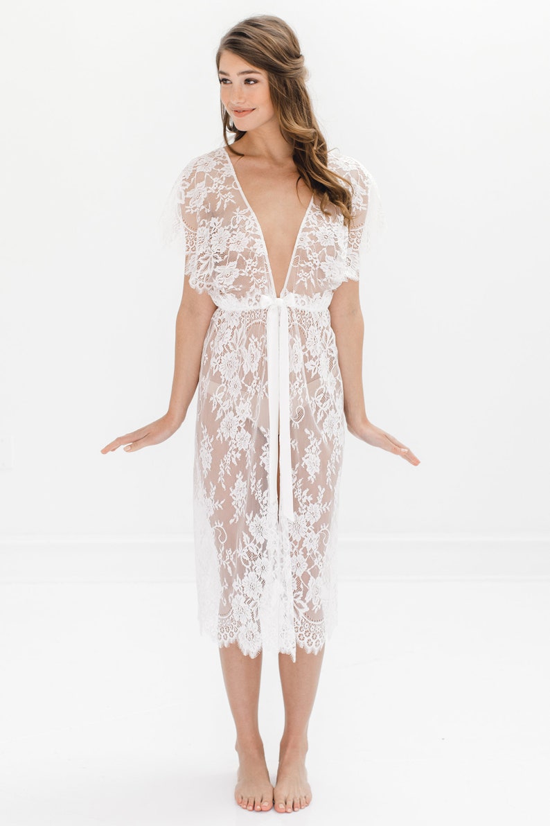 May include: A white lace robe with a deep V-neckline and short sleeves. The robe is tied at the waist with a satin ribbon.