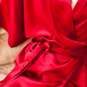 May include: A red satin robe with a self-tie sash. The robe is made of a soft, luxurious fabric and has a relaxed fit.