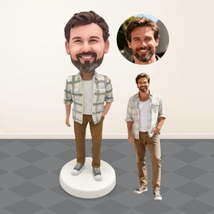 May include: A custom bobblehead figurine featuring a bearded person with brown hair, wearing a white t-shirt, a light-coloured plaid button-down shirt, and brown trousers. The figurine stands on a round white base, accompanied by a reference photo.