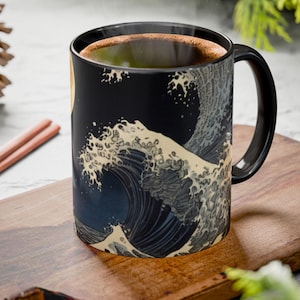 May include: A black ceramic mug featuring a detailed graphic print of a large, stylized ocean wave in shades of cream, grey, and dark blue. The mug has a smooth, cylindrical body with a curved handle on the right side and a dark interior.