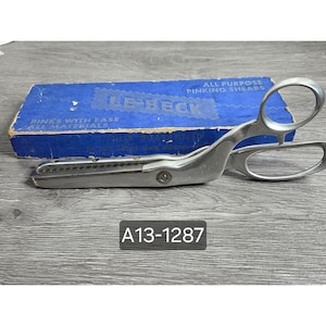 May include: Silver-toned metal Le-Beck pinking shears with serrated blades and two finger loops. The shears are positioned in front of a blue rectangular cardboard box labeled All Purpose Pinking Shears, Pinks With Ease All Materials.