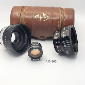 Puede incluir: Un conjunto de lentes de cámara y una funda de cuero marrón. Las lentes son negras con marcas plateadas y blancas, y la funda tiene una cremallera y la palabra "ALPEX" en relieve. El texto "TELEPHOTO LENS" es visible.