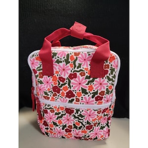 May include: A small, floral-patterned backpack with a white zipper and red handles. The bag features a repeating pattern of pink, orange, and red flowers on a white background. The handles are a solid red color.