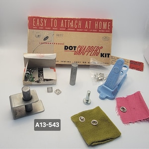 May include: A vintage Dot Snappers Kit with various tools and components for attaching snaps to fabric. The kit includes a blue Gripper tool, metal pieces, and a box with the text "EASY TO ATTACH AT HOME".