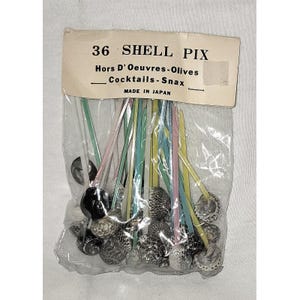 May include: A package of 36 shell picks for hors d'oeuvres, olives, cocktails, and snacks. The picks have colorful stems and shell-shaped tops. The packaging includes text that reads "36 Shell Pix" and "Made in Japan."