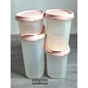 Può includere: Un set di quattro contenitori per alimenti in plastica traslucida con coperchi rosa chiaro. I contenitori variano in altezza, con due unità rettangolari più alte e due più corte. Ogni coperchio ha un meccanismo di chiusura. Il testo A10-1304 è visibile.