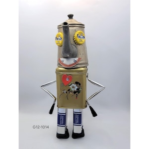 May include: A whimsical robot sculpture crafted from repurposed metal objects. The head is a vintage tea kettle with bottle cap eyes, a spout nose, and a painted smile. The body is a gold tin with a heart and floral design. The arms are metal rods, and the legs are made from cigarette boxes.