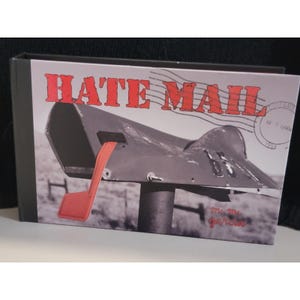 Puede incluir: Una portada de libro con las palabras "HATE MAIL" en rojo. La imagen presenta una fotografía en blanco y negro de un buzón con una bandera roja. Las palabras "Mr. & Mrs. Garcia" están escritas en cursiva.