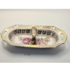 May include: A vintage porcelain serving dish, oval in shape, with a gold handle and trim. It features a floral design with pink roses and yellow accents. The text "G11-860" is printed on the side.