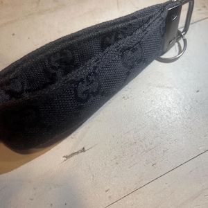 May include: A black fabric key pouch with a repeating pattern. The pouch has a metal clasp and a key ring attached. The fabric appears to be a woven material.
