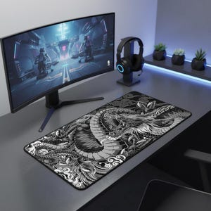 Puede incluir: Alfombrilla de ratón para juegos en blanco y negro con un diseño de dragón. La alfombrilla rectangular está sobre un escritorio gris, con un monitor de ordenador y auriculares en el fondo. El diseño del dragón es detallado y estilizado.