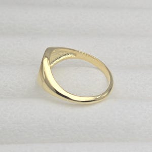 May include: A gold ring with a rectangular face. The ring is made of polished gold and has a smooth, rounded band. The face of the ring is slightly raised and has a flat surface.