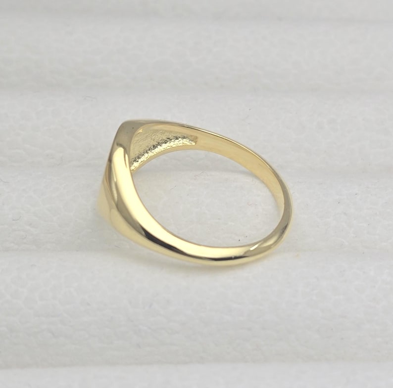 May include: A gold ring with a rectangular face. The ring is made of polished gold and has a smooth, rounded band. The face of the ring is slightly raised and has a flat surface.