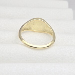May include: A gold-colored ring with a smooth, oval-shaped face. The ring has a simple, classic design, and the band is rounded. The ring is likely made of gold or a gold-colored metal. The ring is a piece of jewelry.