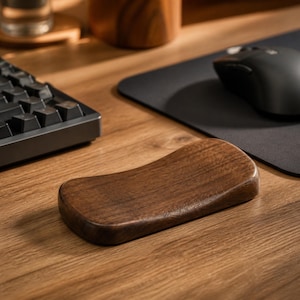 Op de afbeelding: Een donkerbruine houten polssteun met een glad, gecontourd oppervlak en een gebogen ergonomische vorm. Het rechthoekige accessoire heeft een natuurlijk houtnerfpatroon en een gepolijste afwerking, ontworpen om de polsen te ondersteunen.