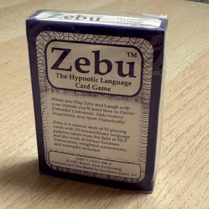 Peut inclure: Un jeu de cartes "Zebu" scellé. La boîte est violet foncé avec du texte blanc qui dit "Zebu The Hypnotic Language Card Game". Le dos de la boîte contient du texte décrivant les caractéristiques du jeu et l'ISBN.