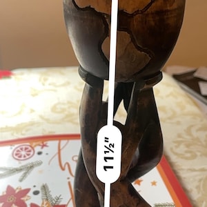 May include: A wooden sculpture of the Earth held by two hands. The sculpture is approximately 29 cm tall and features a detailed carving of the continents. The wood has a dark brown finish.