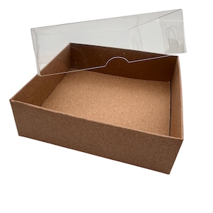 May include: A rectangular brown cardboard box with a clear plastic lid. The lid is partially open, revealing the interior of the box. The box is designed for packaging and storage.