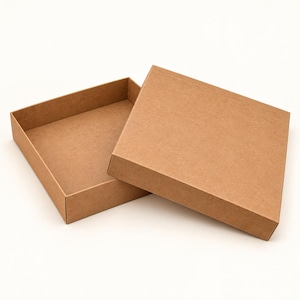 May include: A square, light brown cardboard box with a separate lid. The box is open, revealing a hollow interior, while the lid is positioned partially overlapping the base, showing a simple, flat, and unadorned construction.