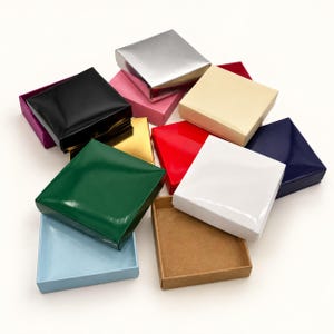 May include: A collection of square gift boxes in various colors including silver, black, pink, cream, red, white, dark blue, green, light blue, and gold. One box is open, revealing a plain brown cardboard interior base.