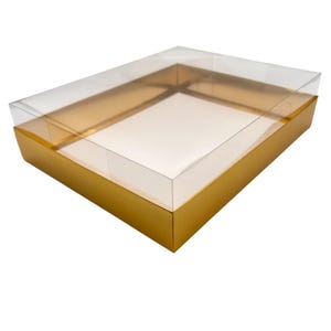 May include: A rectangular gift box with a clear plastic lid and a gold-colored base. The box is empty and sits on a white background. The lid is slightly ajar, revealing the interior of the box.