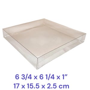 May include: A clear, square plastic box with a lid. The box measures 6 3/4 x 6 1/4 x 1 inches. The text on the image reads "6 3/4 x 6 1/4 x 1" and "17 x 15.5 x 2.5 cm".