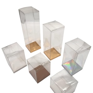 Puede incluir: Conjunto de cajas de plástico transparente de diversas formas y tamaños. Algunas tienen bases doradas o iridiscentes, otras son lisas. Diseñadas para embalaje o exhibición.