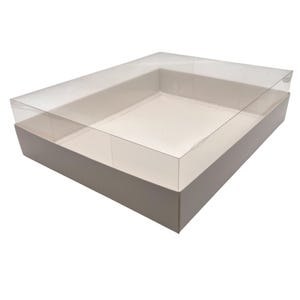 May include: A rectangular, two-piece box with a clear plastic lid and a light beige base. The lid fits snugly over the base, creating a secure closure. The box is designed for packaging and presentation of various items.