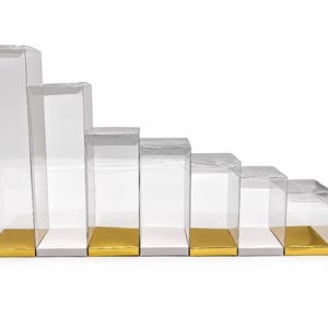 May include: A set of eight clear rectangular plastic display boxes arranged in descending order of height. Each box features a solid base, alternating between a reflective metallic gold finish and a plain white finish for the bottom panel.