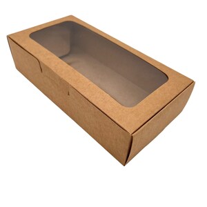 May include: A rectangular brown cardboard box featuring a clear plastic window on the top lid. The box is constructed from a single piece of folded paper material with a smooth finish, designed with a hinged lid and a hollow interior space.