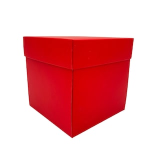 Peut inclure: Une boîte cadeau carrée rouge vif avec un couvercle assorti. La boîte est vide et se détache sur un fond blanc. Elle est faite d'un matériau robuste et présente des bords nets et précis.