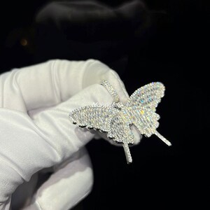 May include: A sparkling butterfly pendant, encrusted with numerous clear gemstones. The butterfly design features detailed wings and antennae, creating a dazzling effect. The jewelry is set against a dark background.