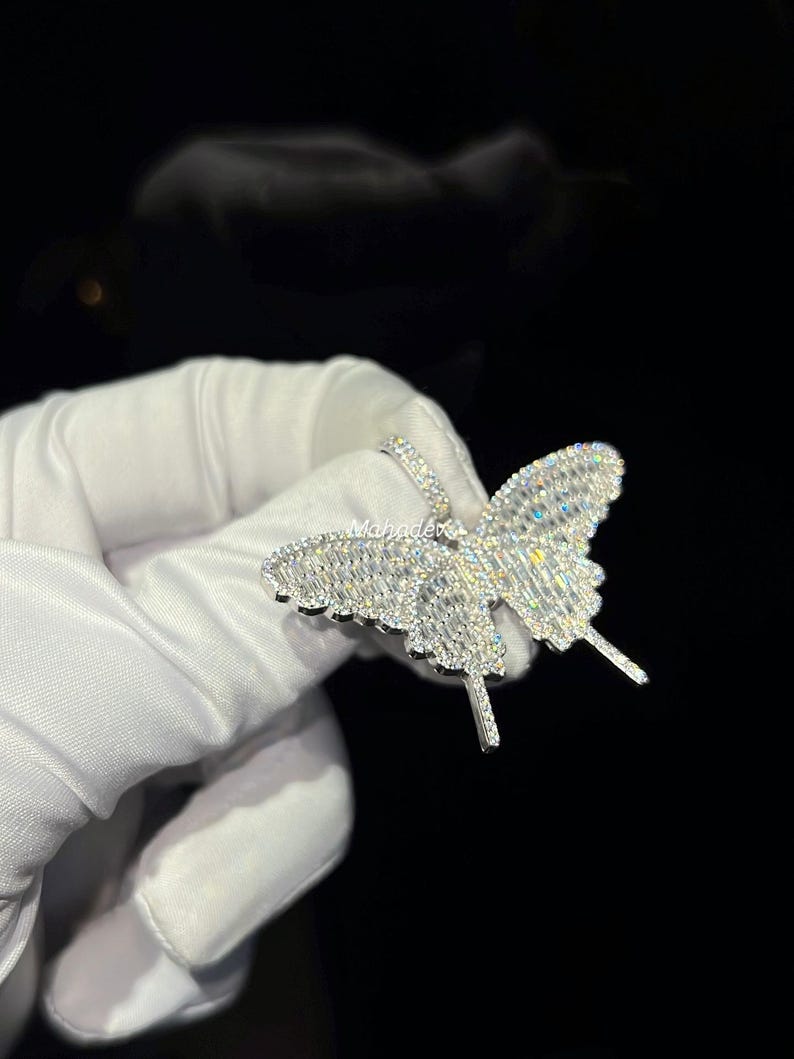 May include: A sparkling butterfly pendant, encrusted with numerous clear gemstones. The butterfly design features detailed wings and antennae, creating a dazzling effect. The jewelry is set against a dark background.