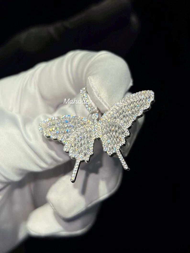 May include: A sparkling butterfly pendant, encrusted with numerous small, clear gemstones. The pendant's wings are spread wide, showcasing the intricate design and reflecting light. The jewelry is held against a dark background.