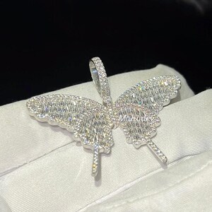 May include: A silver butterfly pendant with a sparkling, gem-studded design. The pendant features a detailed butterfly shape with intricate stone settings, creating a dazzling effect. The pendant has a loop for a chain.