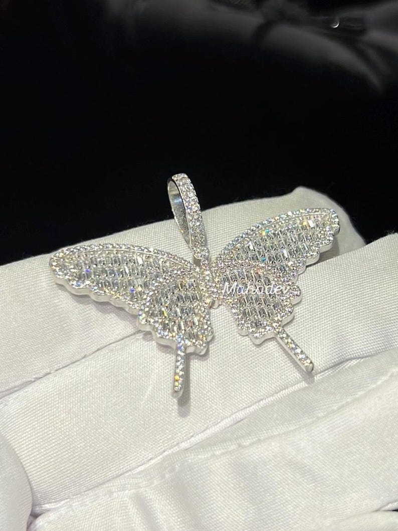 May include: A silver butterfly pendant with a sparkling, gem-studded design. The pendant features a detailed butterfly shape with intricate stone settings, creating a dazzling effect. The pendant has a loop for a chain.